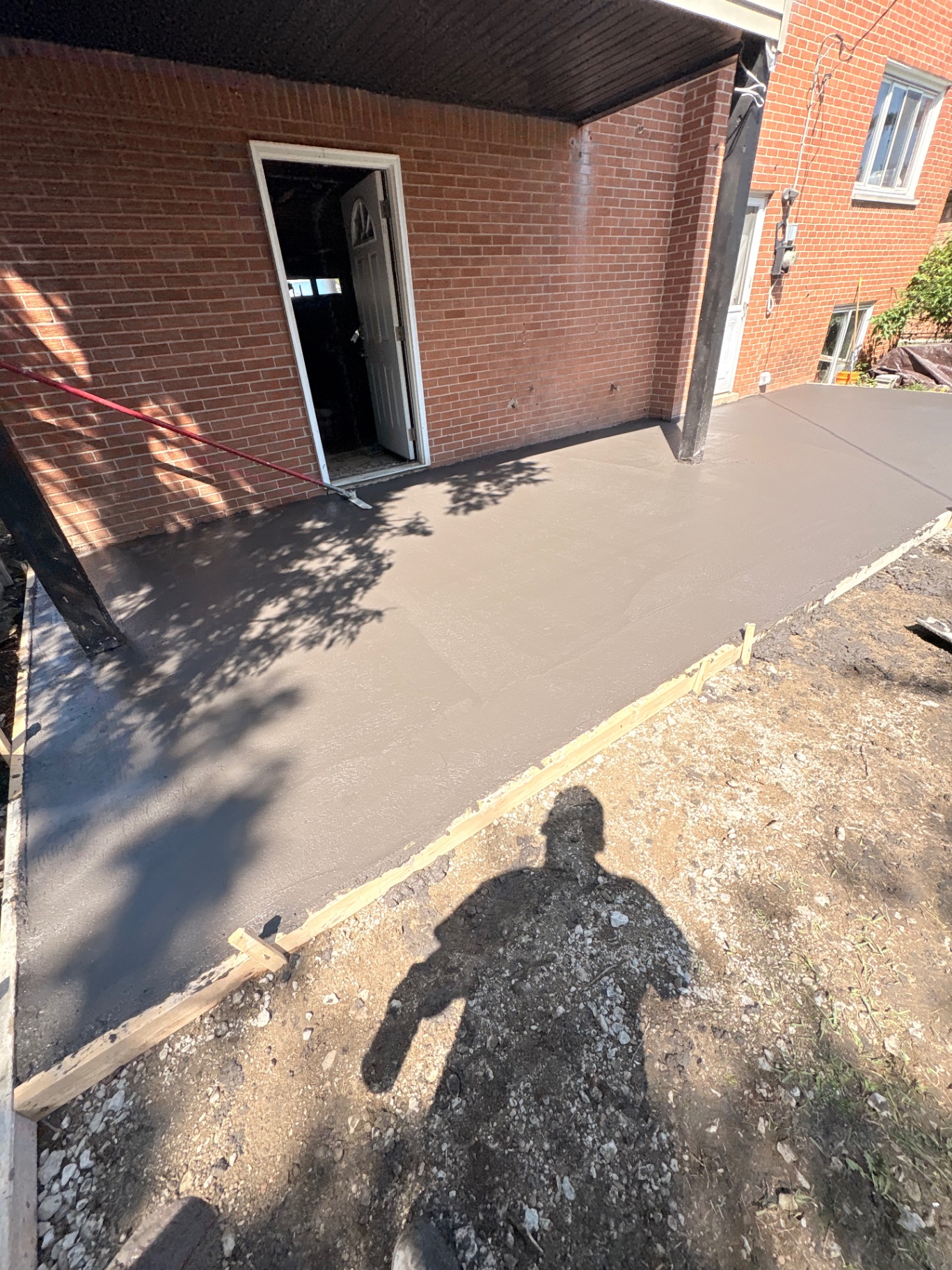Freshly poured covered patio slab beside a brick home