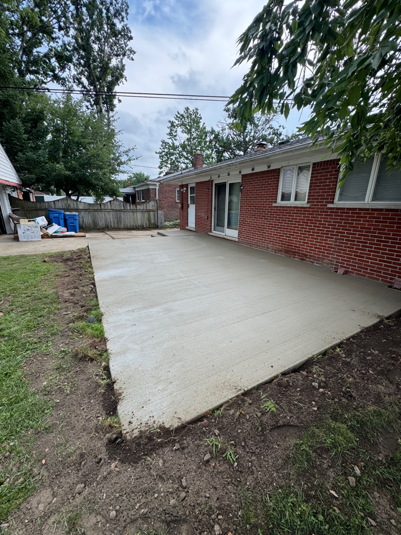 Freshly finished backyard concrete patio behind a brick home